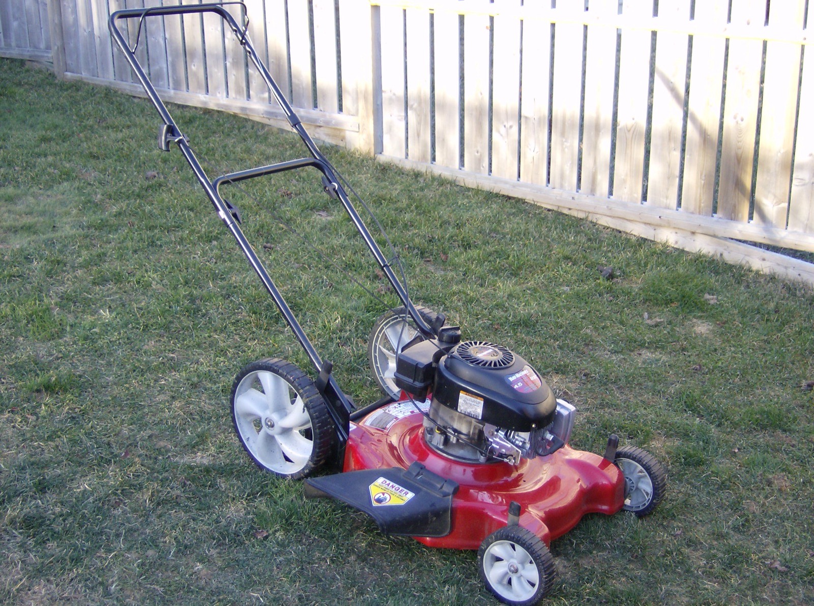 A push mower parked on a lawn beside a wooden fence